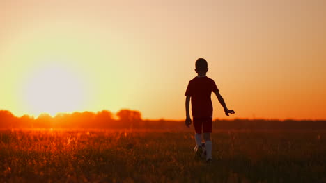 Siguiendo-A-Un-Jugador-De-Fútbol-Con-Una-Camiseta-Roja-Y-Pantalones-Cortos-Corriendo-Con-El-Balón-Al-Atardecer-En-El-Campo-Sobre-El-Césped.-El-Concepto-De-Jugadores-Jóvenes.-El-Joven-Futbolista-Sueña-Con-Una-Carrera-Profesional-Y-Se-Entrena-En-El-Campo.